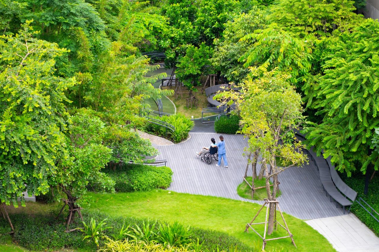 A young nurse pushes a patient's wheelchair out into the hospital's wide garden for fresh air