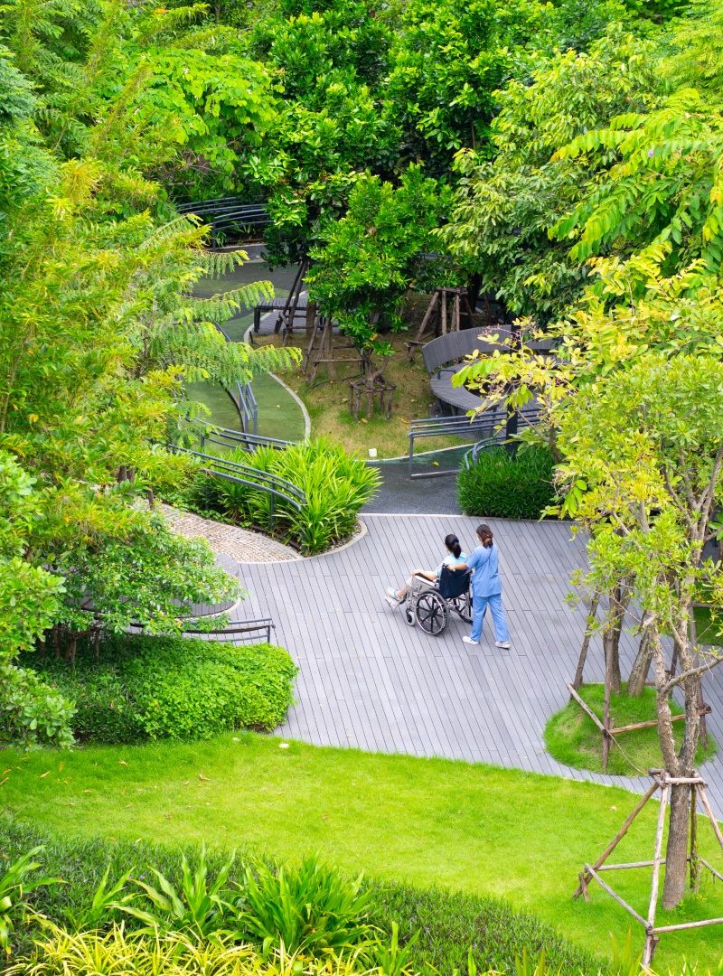 A young nurse pushes a patient's wheelchair out into the hospital's wide garden for fresh air.